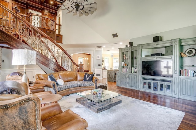 living area with arched walkways, a decorative wall, wood finished floors, a towering ceiling, and stairway