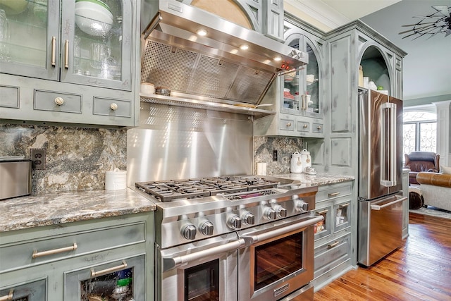 kitchen with wall chimney exhaust hood, premium appliances, decorative backsplash, and gray cabinetry