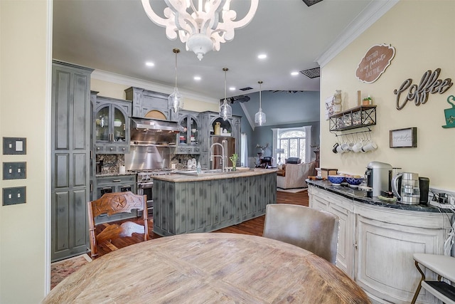 kitchen featuring a center island with sink, glass insert cabinets, wood finished floors, crown molding, and stainless steel stove