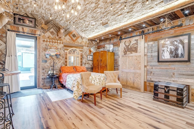 bedroom with access to outside, wood finished floors, wood walls, and a barn door