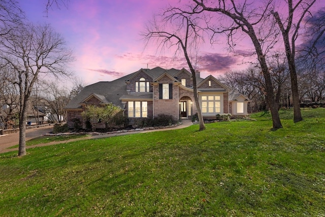 french country inspired facade with brick siding, a chimney, and a front yard