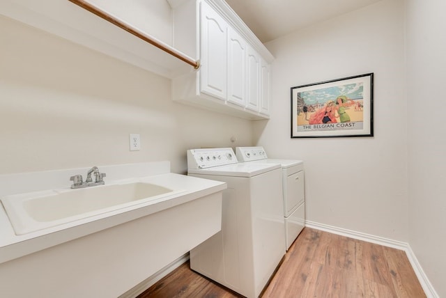 laundry area featuring cabinet space, light wood-style floors, washing machine and dryer, a sink, and baseboards