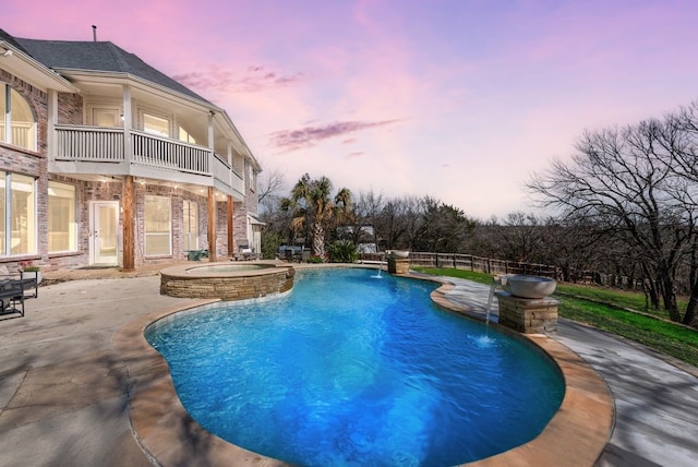 pool at dusk with a patio area, fence, and a pool with connected hot tub