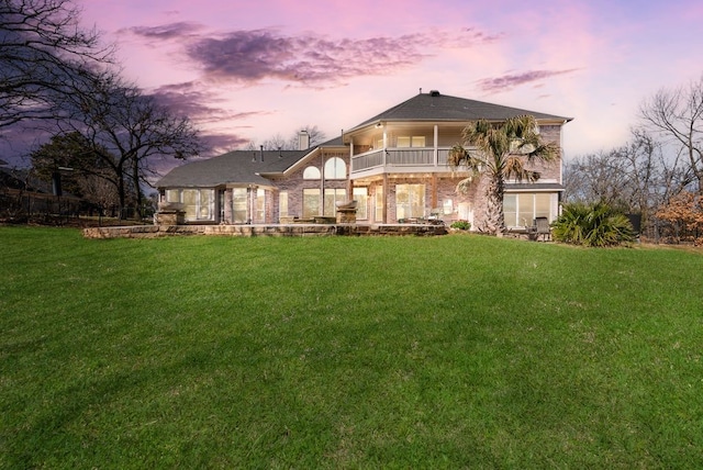 back of house at dusk featuring a balcony, a patio area, and a lawn