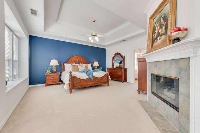 bedroom featuring light carpet, a tiled fireplace, a raised ceiling, and visible vents