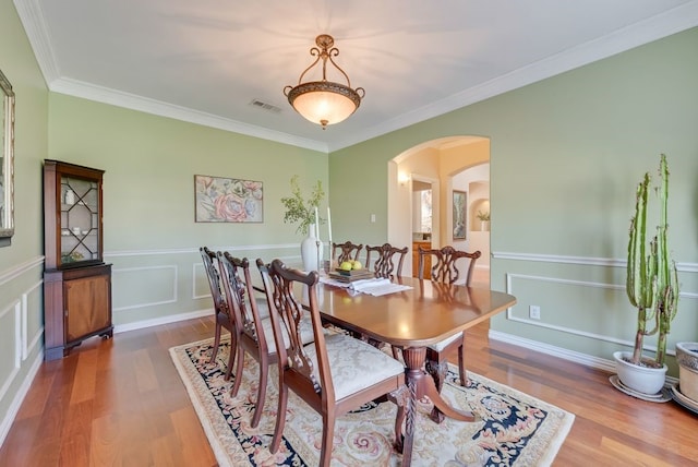 dining area featuring visible vents, arched walkways, a wainscoted wall, ornamental molding, and wood finished floors