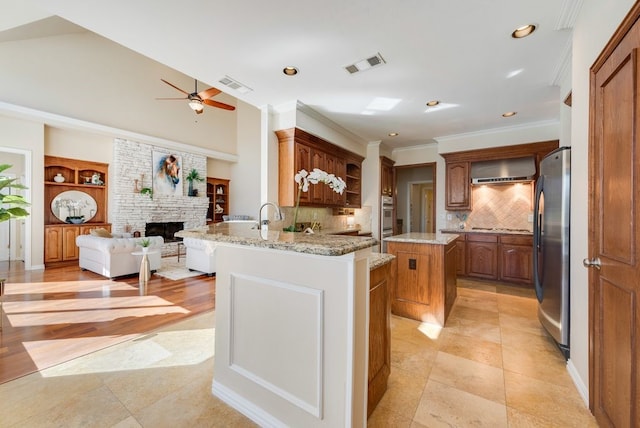 kitchen with visible vents, a peninsula, stainless steel appliances, wall chimney range hood, and a fireplace