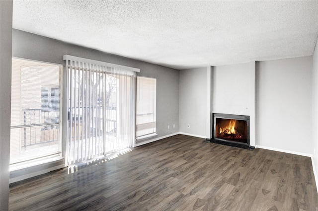 unfurnished living room with a warm lit fireplace, a textured ceiling, baseboards, and wood finished floors