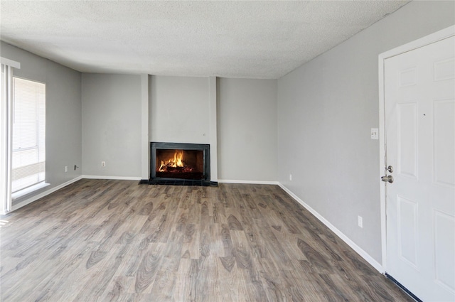 unfurnished living room featuring a lit fireplace, a textured ceiling, baseboards, and wood finished floors