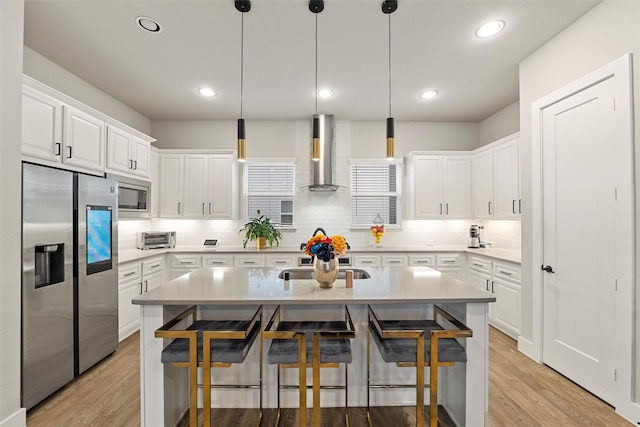 kitchen with a breakfast bar, wall chimney exhaust hood, stainless steel appliances, and light countertops