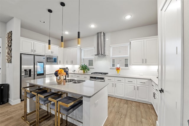 kitchen featuring stainless steel appliances, light wood-style floors, a sink, wall chimney range hood, and a kitchen breakfast bar