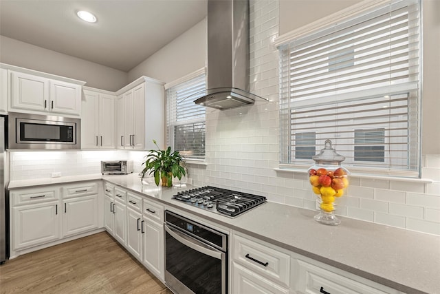 kitchen with light wood-style flooring, stainless steel appliances, white cabinetry, light countertops, and wall chimney range hood