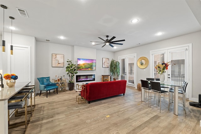 living room featuring a glass covered fireplace, french doors, light wood-style flooring, and visible vents