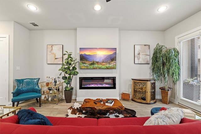 living room featuring a glass covered fireplace, visible vents, recessed lighting, and wood finished floors