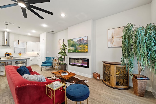 living area featuring a glass covered fireplace, visible vents, light wood finished floors, and recessed lighting