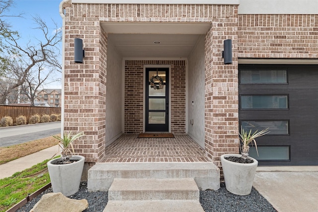 doorway to property with a garage, concrete driveway, and brick siding