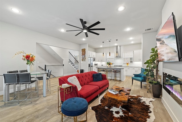 living room with recessed lighting, visible vents, light wood-style floors, ceiling fan, and stairs