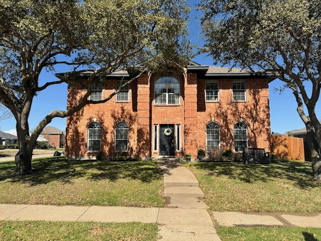 colonial house with brick siding, fence, and a front yard