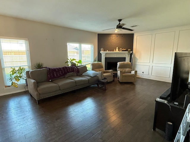 living area with dark wood-style floors, a fireplace, a decorative wall, and a ceiling fan