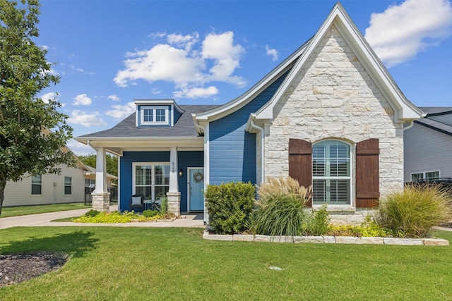 view of front facade featuring a front yard, stone siding, and covered porch