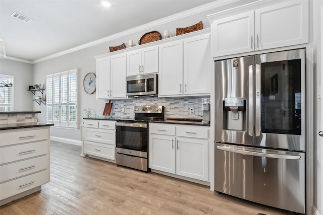 kitchen featuring crown molding, light wood finished floors, visible vents, decorative backsplash, and appliances with stainless steel finishes