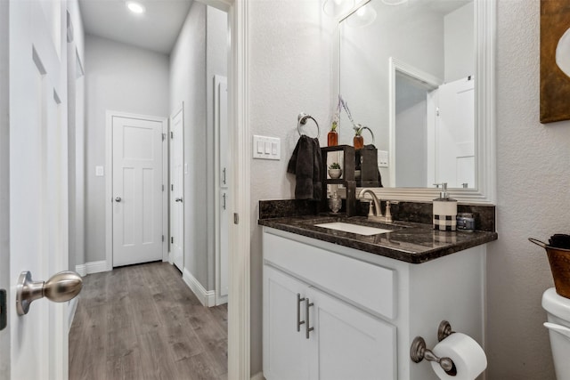 half bathroom featuring toilet, wood finished floors, vanity, and baseboards