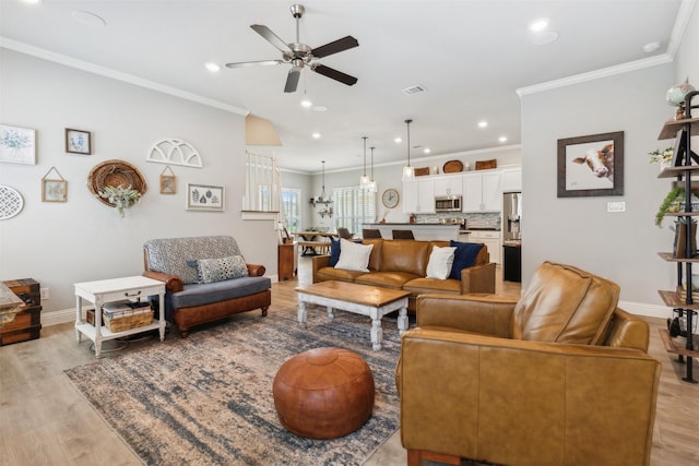 living room with ornamental molding, light wood-type flooring, visible vents, and baseboards