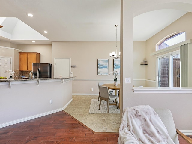 kitchen with stone counters, a breakfast bar, light wood finished floors, recessed lighting, and stainless steel fridge with ice dispenser