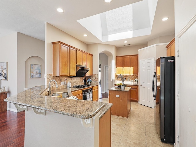 kitchen with light stone counters, arched walkways, a sink, a peninsula, and black appliances