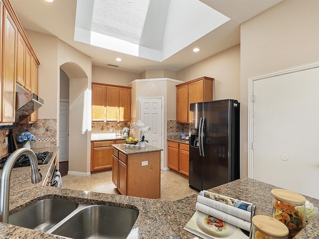 kitchen featuring tasteful backsplash, dark stone counters, a center island, black refrigerator with ice dispenser, and a sink