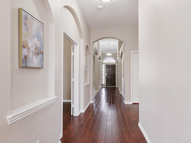 hallway featuring dark wood-style floors, baseboards, and arched walkways