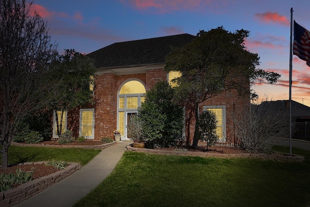 view of front of property with brick siding, a front yard, and a shingled roof