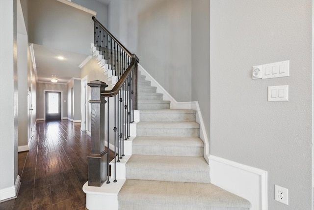 staircase featuring a high ceiling, baseboards, and hardwood / wood-style flooring