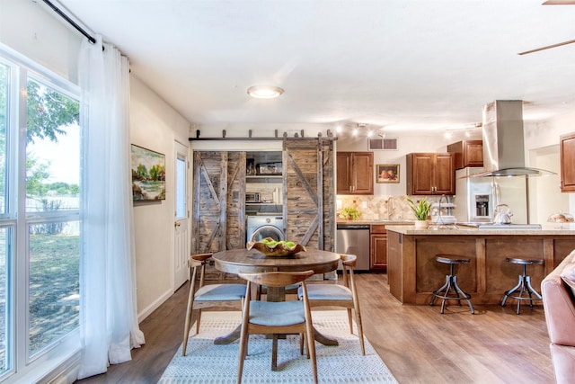 dining space featuring washer / dryer, a barn door, visible vents, and light wood-style floors