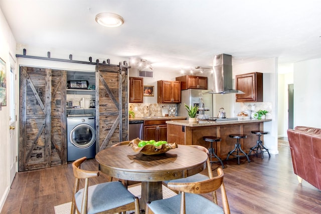 kitchen featuring a barn door, stainless steel appliances, wood finished floors, wall chimney exhaust hood, and washer / clothes dryer