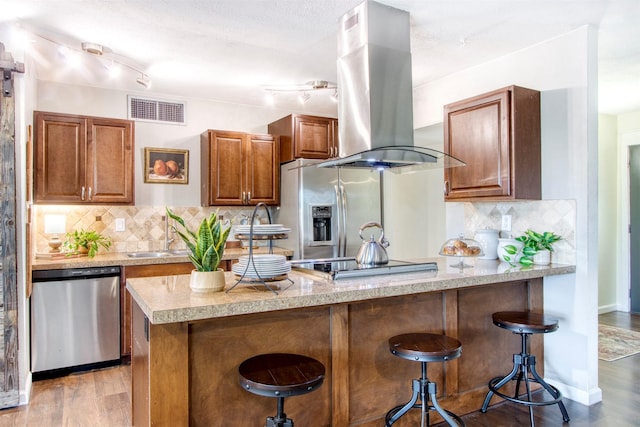 kitchen featuring visible vents, island range hood, light wood-style flooring, a breakfast bar area, and stainless steel appliances