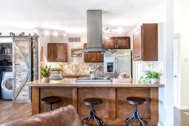 kitchen featuring washer / dryer, a barn door, island range hood, stainless steel fridge with ice dispenser, and a sink