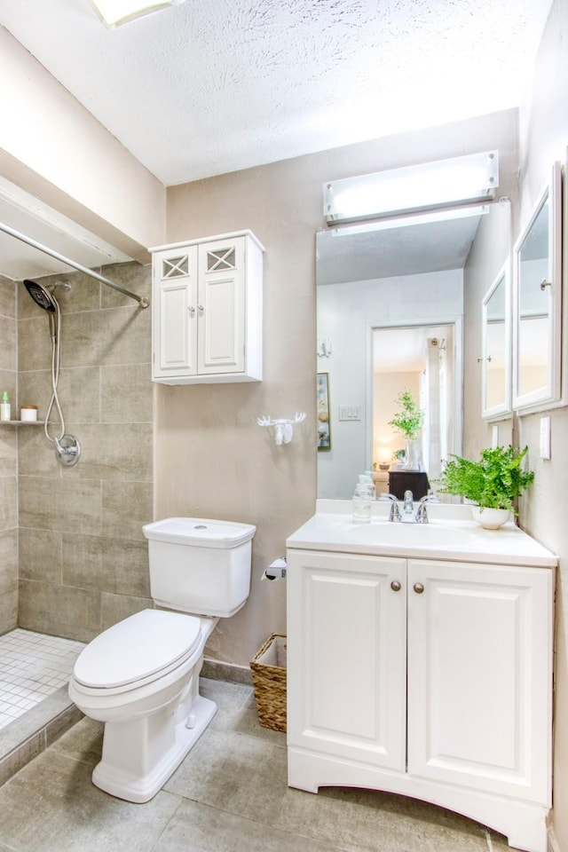 full bath with baseboards, tiled shower, toilet, a textured ceiling, and vanity