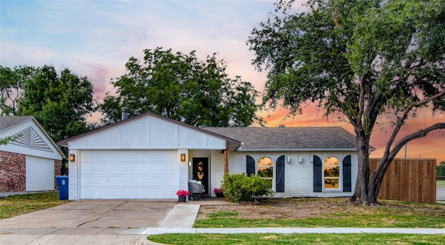 ranch-style house featuring an attached garage, driveway, a shingled roof, and brick siding