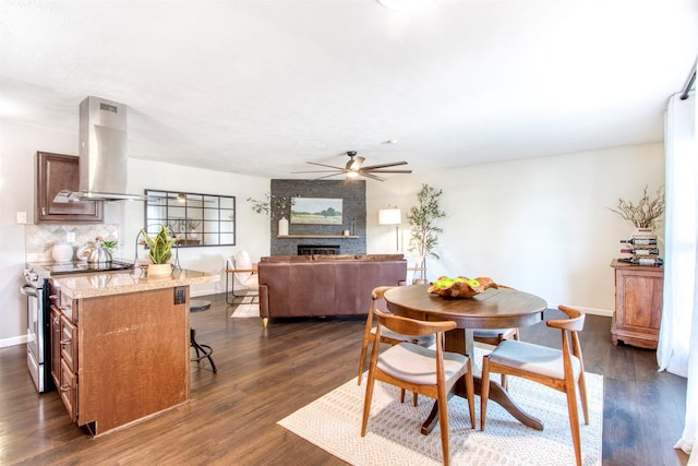 dining area featuring a large fireplace, baseboards, dark wood finished floors, and a ceiling fan