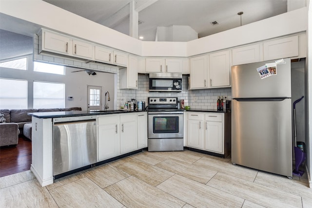 kitchen with a peninsula, a sink, appliances with stainless steel finishes, backsplash, and dark countertops