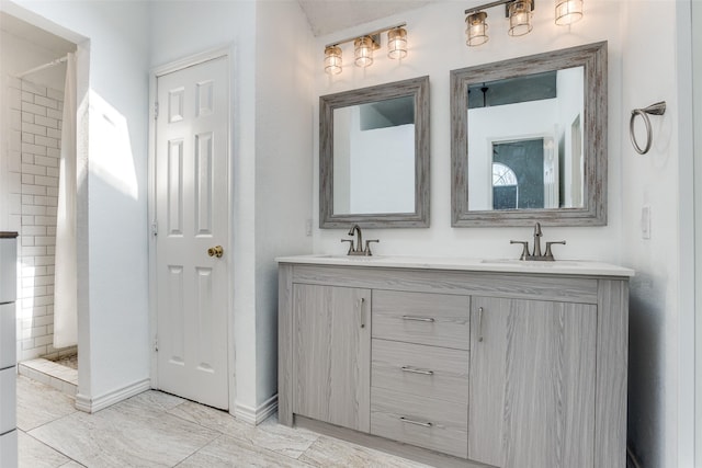 full bathroom featuring double vanity, tiled shower, a sink, and baseboards