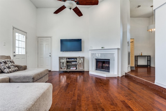 living area featuring a high ceiling, a premium fireplace, visible vents, a ceiling fan, and wood-type flooring