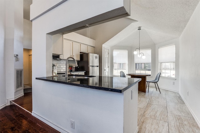 kitchen featuring a peninsula, a sink, visible vents, backsplash, and freestanding refrigerator