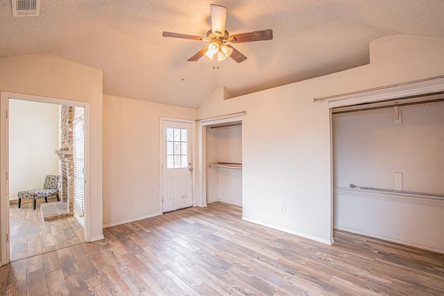 unfurnished bedroom with multiple closets, lofted ceiling, visible vents, a textured ceiling, and light wood-type flooring