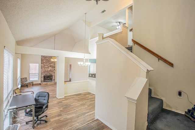 office with a textured ceiling, light wood-style flooring, ceiling fan with notable chandelier, a fireplace, and visible vents