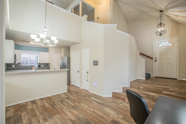 kitchen featuring white cabinets, wood finished floors, a peninsula, stainless steel appliances, and a chandelier