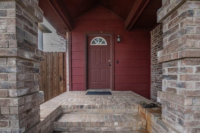 view of exterior entry featuring brick siding and fence