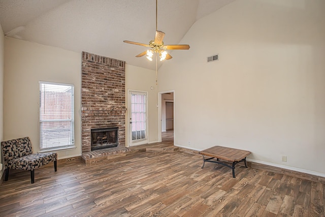 unfurnished room with a healthy amount of sunlight, a brick fireplace, visible vents, and wood finished floors