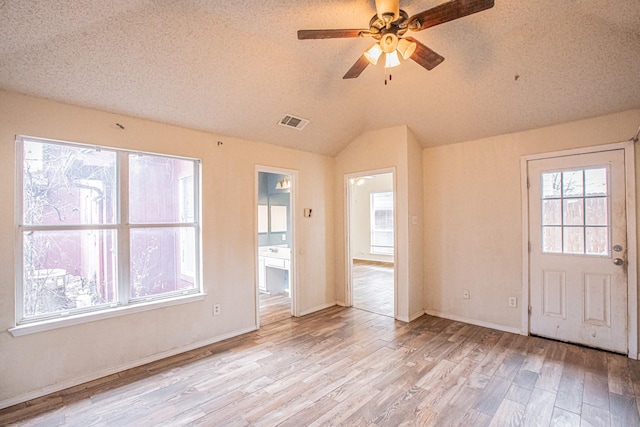 spare room with visible vents, a ceiling fan, lofted ceiling, light wood-style flooring, and a textured ceiling